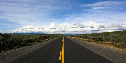 Open road of balck asphalt with yellow line in Eastern Oregon leading to big sky with white clouds...