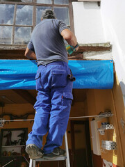 bricklayer construction worker on metal staircase to repair old tile roof and  and pvc gutters to collect rainwater