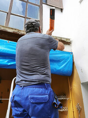 bricklayer construction worker on metal staircase to repair old tile roof and  and pvc gutters to collect rainwater