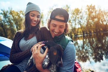 Smile, camping and couple with dog for adventure by love of freedom in nature lake, sunshine and travel, pet or holiday. Happy, woman and man with puppy for care, hug or relax in summer journey - Powered by Adobe