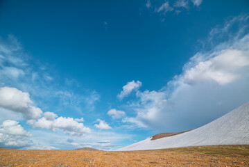 Orange tent on stony mountain pass in bright sun. Glacier on stone hillside under clouds in blue...