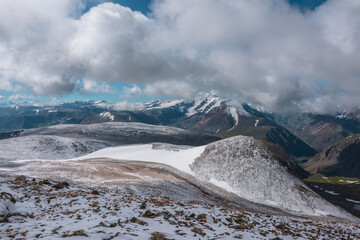 Vast alpine view to snowy stony pass and large mountain range with snow-white peak in far away...