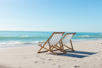 Fototapeta premium At beach, two empty chairs facing ocean, waiting for visitors