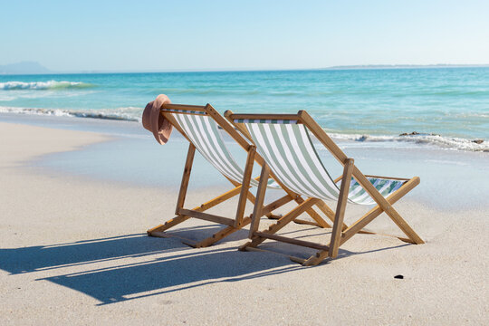 At beach, empty chair with hat on sandy shore, gentle waves touching beach