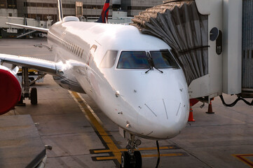 Front view of white modern jet airliner with attached passenger boarding bridge. The plane is sitting on a concrete tarmac with painted lane lines