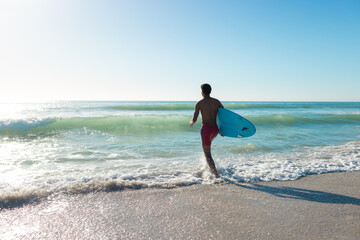 At beach, young biracial man holding surfboard running towards sea