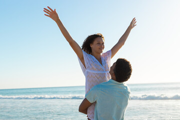 At beach, biracial couple enjoying time, male lifting female