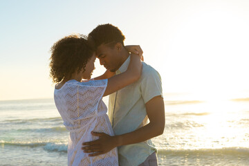 Obraz premium At beach, diverse couple embracing, sunset lighting up sky