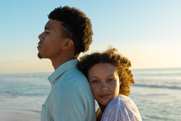 At beach, biracial couple standing, woman leaning on man