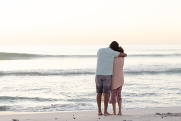 Obraz premium At beach, diverse couple embracing, watching ocean waves