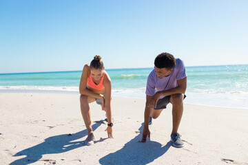 Obraz premium At beach, diverse couple catching breath on sunny day, both looking fit