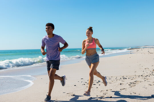 At beach, diverse couple jogging, enjoying exercise - Powered by Adobe