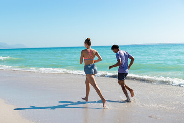 Obraz premium At beach, diverse couple running, holding hands