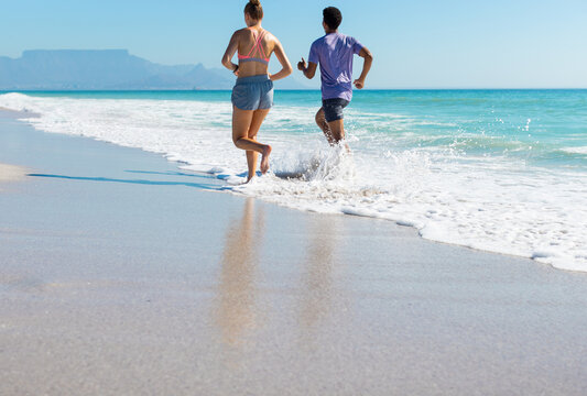At beach, diverse couple running, waves touching their feet
