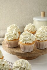 Tasty vanilla cupcakes with cream on white wooden table
