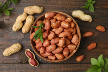 Fresh peanuts and leaves in bowl on wooden table, flat lay