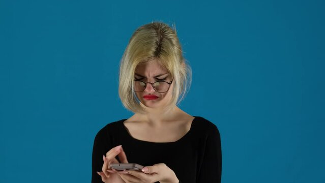 Businesswoman types message with angry face on blue background. Female frustration evident in every keystroke on phone