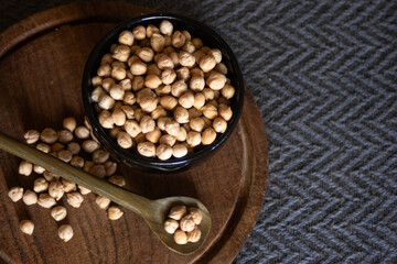 Chickpeas in black bowl and over wooden spoon Dark background. Copy space