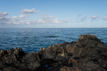 Couple of people stand up paddleboarding in the Pacific Ocean off the black lava rock point on Kamaole Beach Park II at low tide, tropical vacation paradise, Maui, Hawaii
