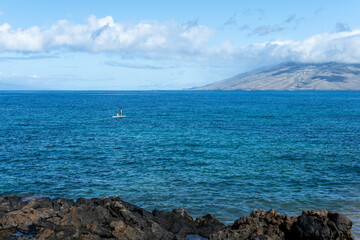 Couple of people stand up paddleboarding in the Pacific Ocean off the black lava rock point on Kamaole Beach Park II at low tide, tropical vacation paradise, Maui, Hawaii
