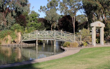 Wooden bridge spanning a serene pond of water surrounded by trees and plants at Riverside Park in Swan Hill, Victoria, Australia