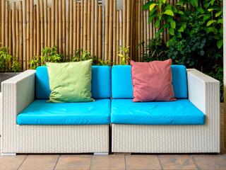 Empty white modern rattan couch seat with blue cushion, sofa with pillows for guests on bamboo wall...
