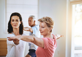 Mature woman and yoga instructor helping with warrior pose at fitness class for exercise...