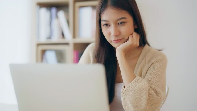 Young asian woman working at home. Happy female using computer laptop on desk at house