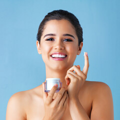 Happy woman, portrait and cream with skincare in satisfaction for facial on a blue studio...