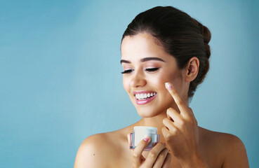 Happy woman, lotion and skincare with container for facial treatment on a blue studio background....