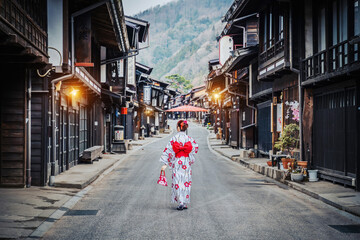 Asian woman wearing a traditional Japanese kimono holds an umbrella at Narai Juku in Nagano, Japan. Translation Narai Juku Village..