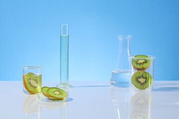Frontal shot photography on blue background with gradient effect, measuring cylinder and erlenmeyer flask filled with transparent liquid, kiwi contained in beaker and petri dish. Displaying space