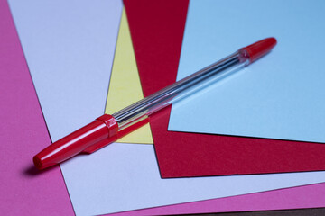 Generic red ballpoint pen sitting on several sheets of colored paper.