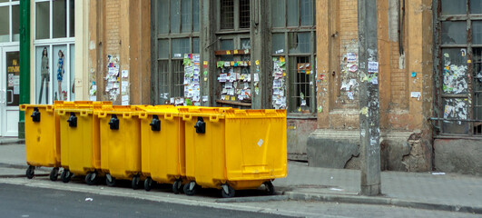 Yellow trash containers on a city street. Five trash cans on city sidewalks.