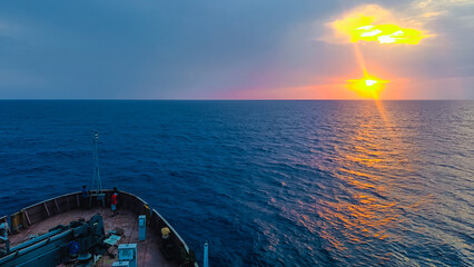ship sailing in blue sea during sunset or sunrise. Golden light of sun reflecting on ocean surface.