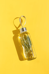 Water bottle, drink detox with rosemary green herb, shadow at sunlight on yellow background....