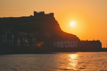 A seaside village with a historic castle on a hill, silhouetted against the setting sun - Powered by Adobe