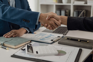 Businessmen shaking hands with sales reports and analysis documents shaking hands while coming to a...