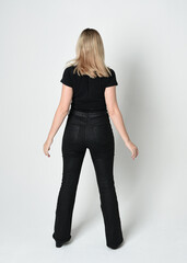 Full length portrait of beautiful blonde woman wearing modern black shirt and leather pants. Confident  standing pose walking away from camera, silhouetted on white studio background.