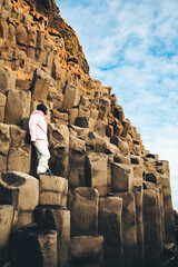 Adult caucasian woman tourist in yellow jacket standing on basalt columns on Reynisfjara Black Sand...