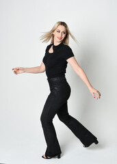 Obraz premium Full length portrait of beautiful blonde woman wearing modern black shirt and leather pants. Confident standing pose with gestural hands presenting, silhouetted on white studio background.