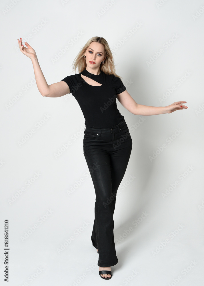 Sticker Full length portrait of beautiful blonde woman wearing modern black shirt and leather pants. Confident standing pose with gestural hands presenting, silhouetted on white studio background.