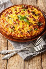 Delicious breakfast omelette with chicken, cheese, bacon and herbs close-up in a plate on the table. Vertical