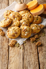 Pumpkin cookies with white chocolate chips, walnut and pumpkin seeds closeup on the parchment on the wooden table. Vertical