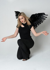 Full length portrait beautiful blonde girl wearing modern black shirt, leather pants, feather angel...