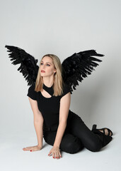 Full length portrait beautiful blonde girl wearing modern black shirt, leather pants, feather angel...