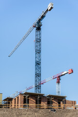 A Pair Of Building Tower Cranes Working In Construction Site On Blue Sky Background