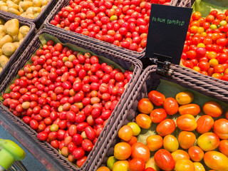 variety of tomatoes displayed in baskets at what appears to be a market. The tomatoes are of different types and colors, indicating a variety of species or ripeness levels. There are four baskets visi