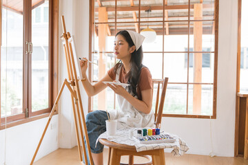 Asian young talented woman artist coloring on painting board in house. Attractive beautiful female draw art picture, creating artwork with watercolor paint and brush enjoy creativity activity at home © photo3idea