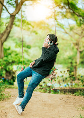 Young man sitting on a swing calling on the phone in a garden. Happy man swinging talking on the phone